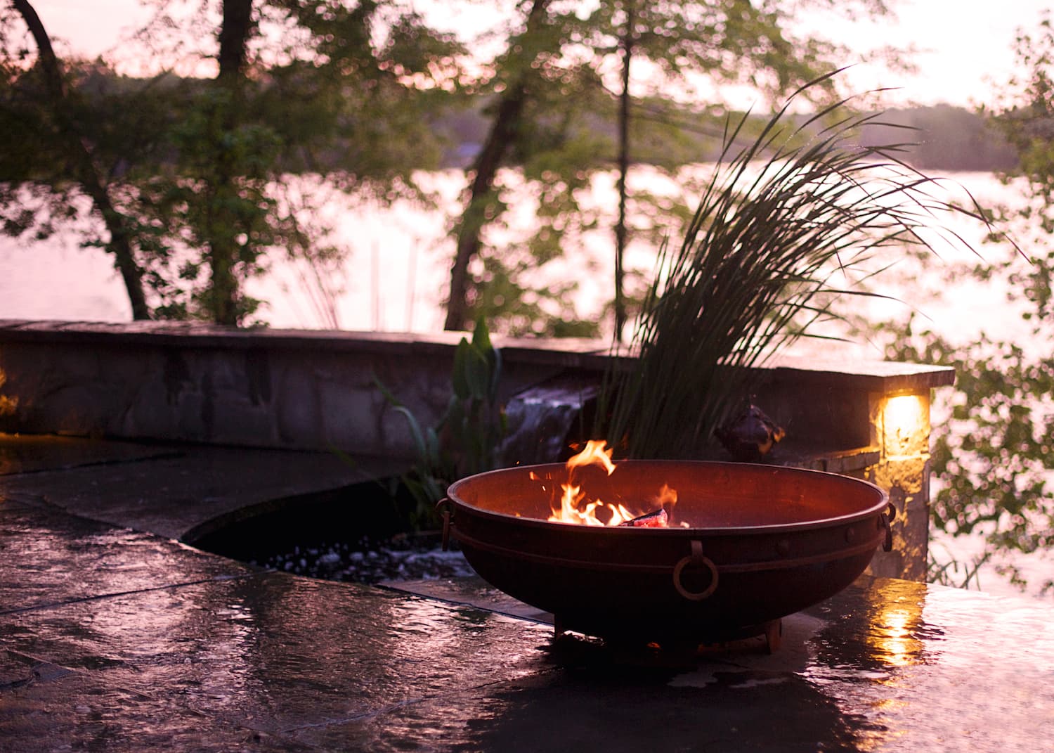 Fire Pit Art's Emperor 37" carbon steel fire pit by a lake with trees and a beautiful sunset in the background.  USA made and fit for a King...or Queen.