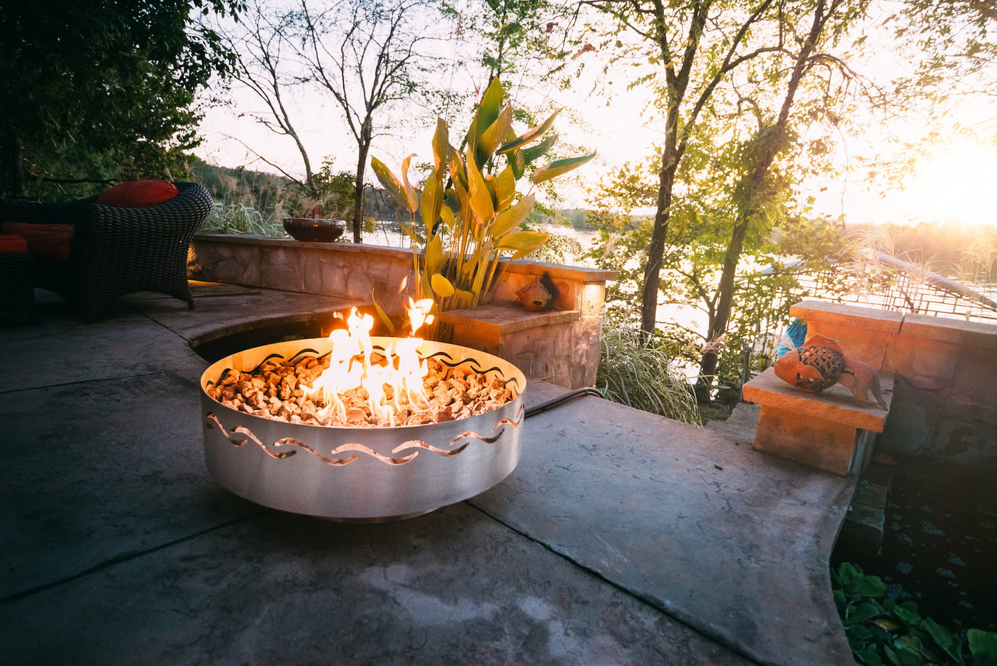 Fire Surfer fire pit burning on lakeside patio surrounded by trees.