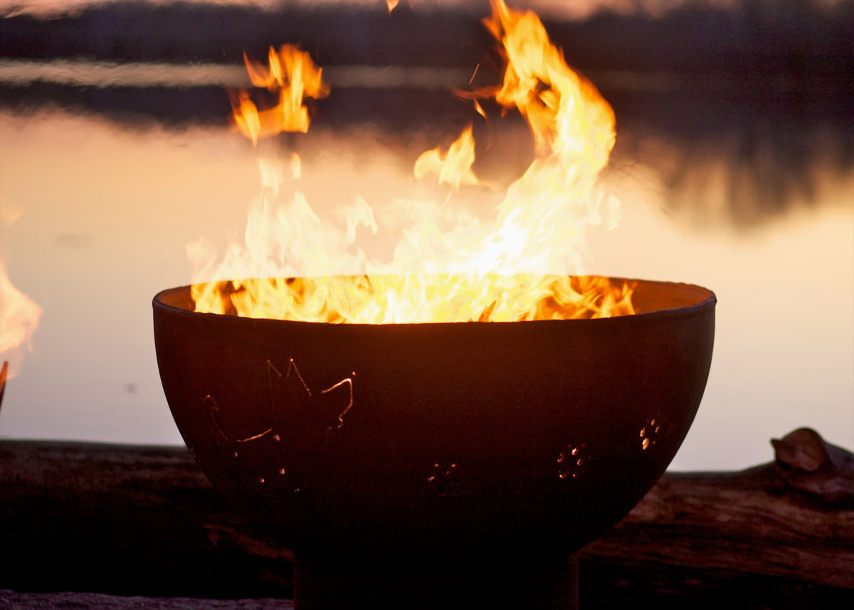 Side profile of Funky Dog 36" carbon steel fire pit featuring metal dog cutouts and even flames with twilight sky.