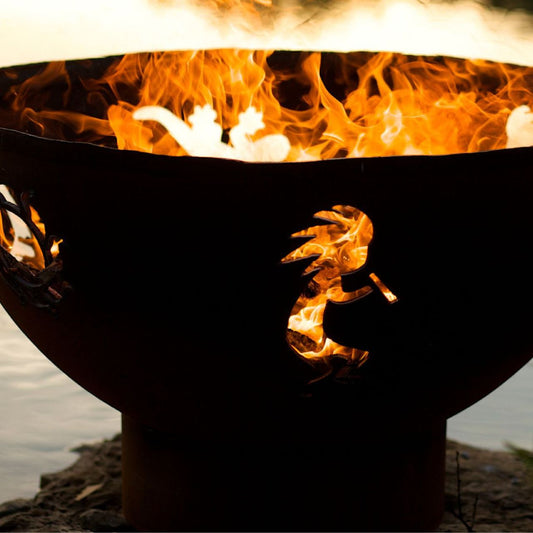 Fire Pit Art's Kokopelli 36" carbon steel fire pit with flames emerging through sunburst and Kokopelli cutouts.