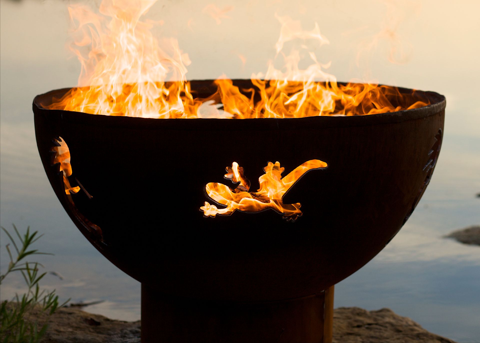 Lakeside Kokopelli 36" carbon steel fire pit with gecko design glowing with fire.