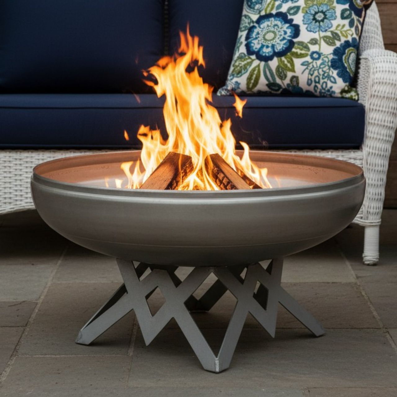 The Liberty Fire Pit - Angular Base - with flames in an patio setting in front of a couch and pillows.