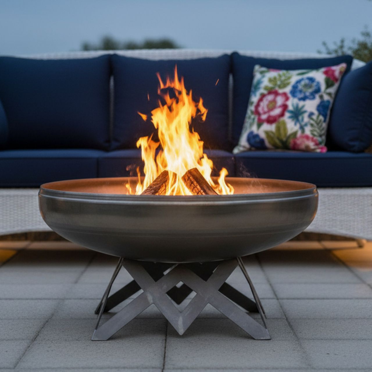 The Liberty Fire Pit - Angular Base - with flames in an patio setting in front of a couch and pillows.