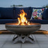 The Liberty Fire Pit - Angular Base - with flames in an patio setting in front of a couch and pillows.
