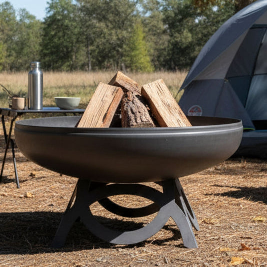 The Liberty Fire Pit - Curved Base - with wood and camping gear in a natural setting.