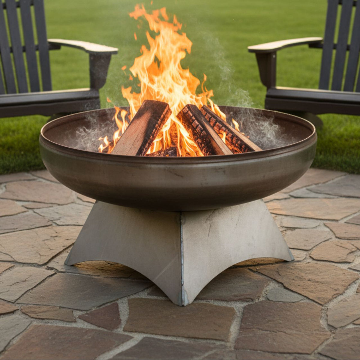 The Liberty Fire Pit - Standard Base - with flames in a backyard setting with chairs and grass.