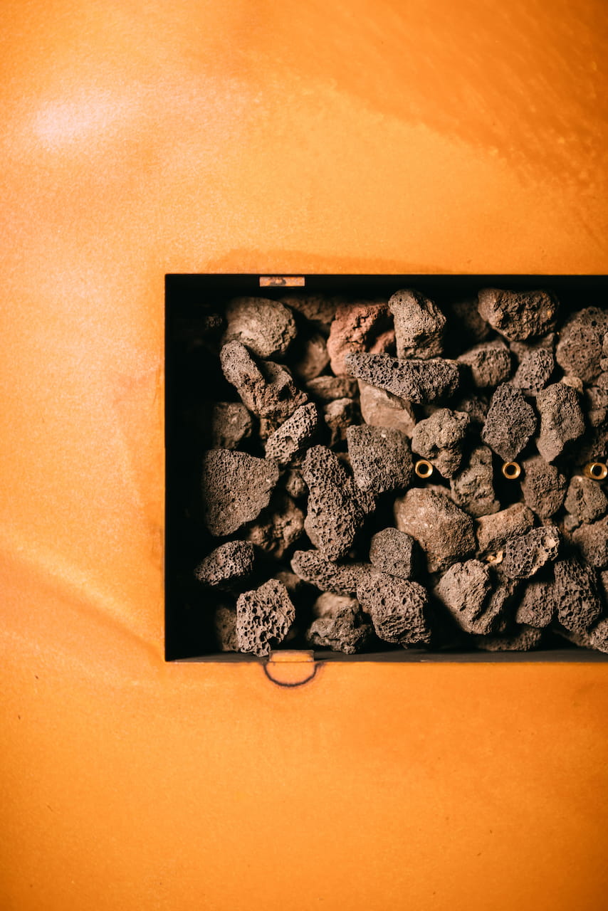 Detailed view of lava rocks and brass gas burner jets inside the Linear fire pit table.