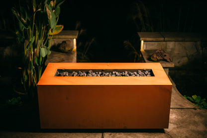 Fire Pit Art's Linear fire pit table with lid off sitting on a patio in the evening.