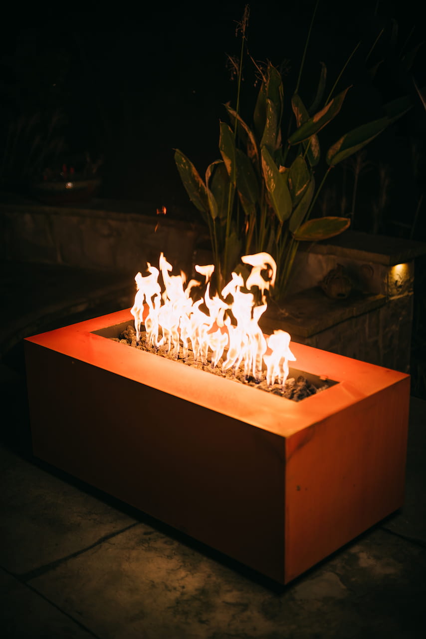 Angled view of Fire Pit Art's Linear fire pit table with flames burning in a dark setting.