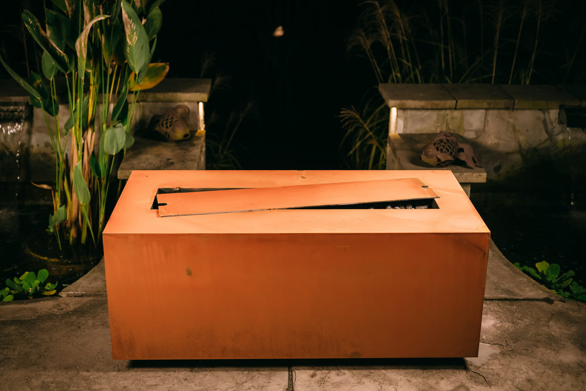 Linear fire pit table with matching steel lid placed across the opening sitting on a patio in the evening.