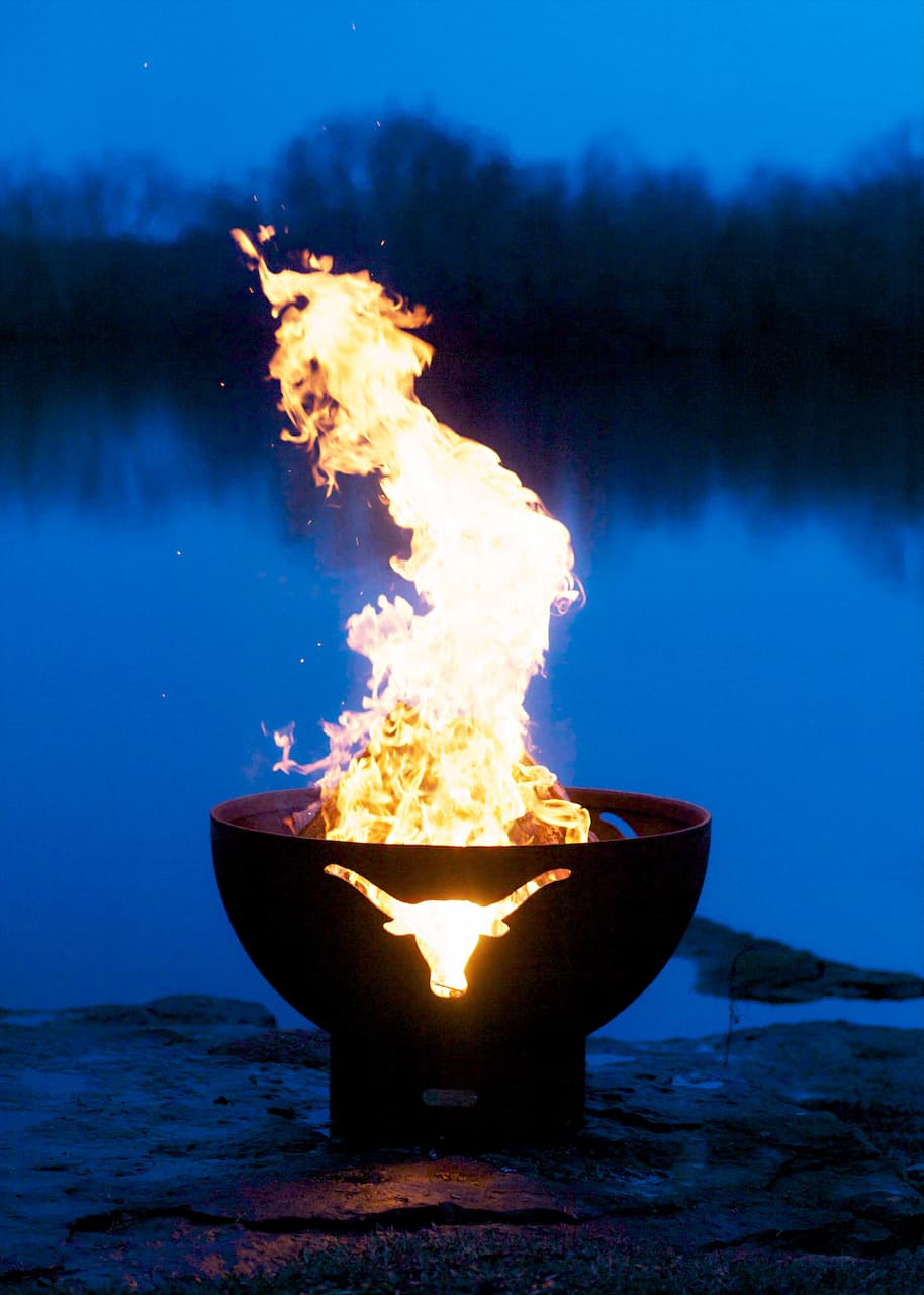 Long Horn 36" carbon fire pit with flame rising through steel cutout of a longhorn silhouette against a deep blue sky.