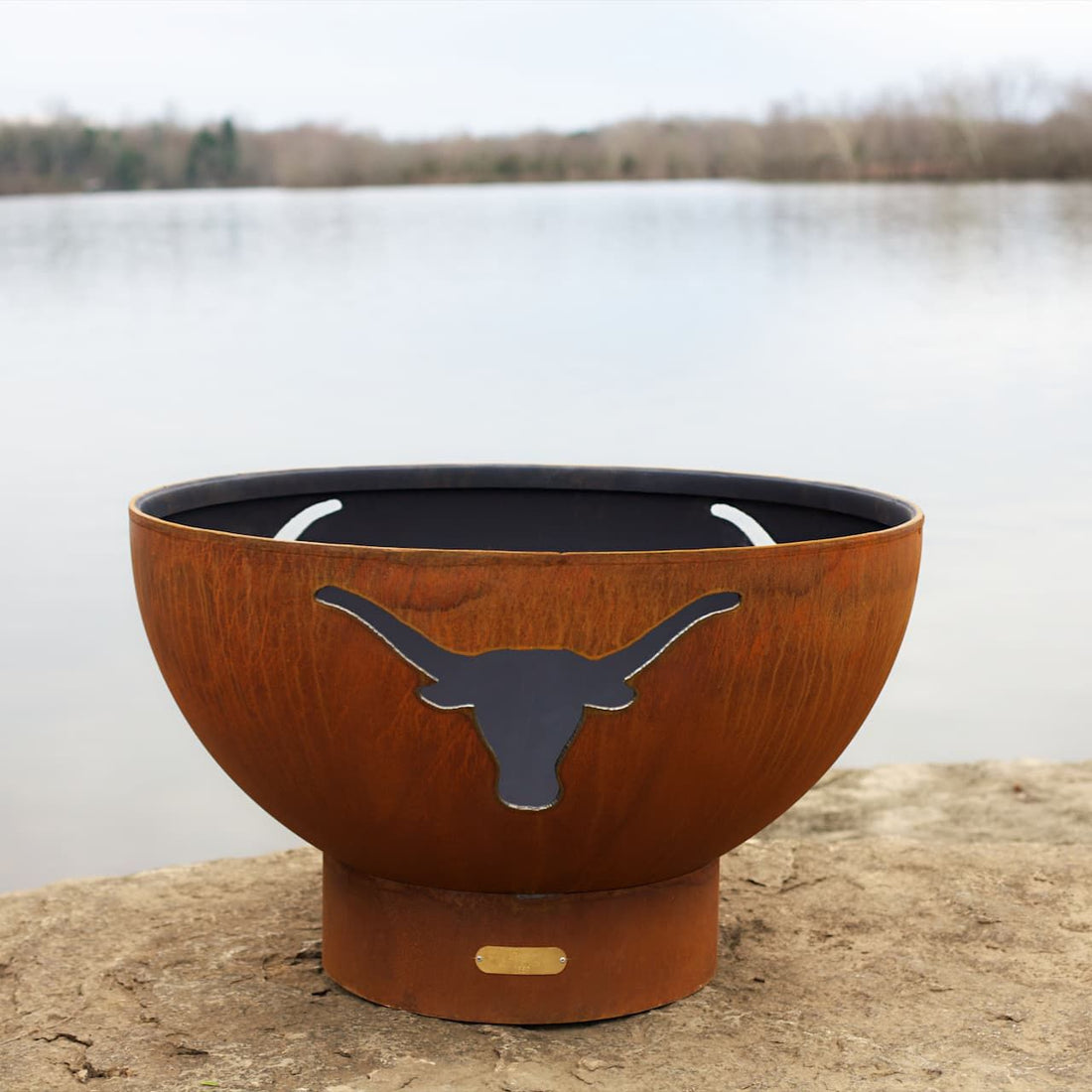 Long Horn 36″ Carbon Steel Fire Pit with weathered patina next to a body of water. 