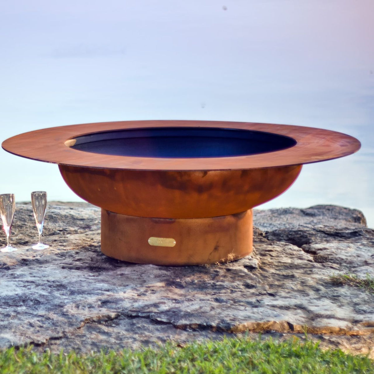 Magnum 54" carbon steel fire pit placed on stone cliff edge at sunset.  Made in USA by Fire Pit Art.