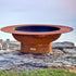 Magnum 54" carbon steel fire pit placed on stone cliff edge at sunset.  Made in USA by Fire Pit Art.