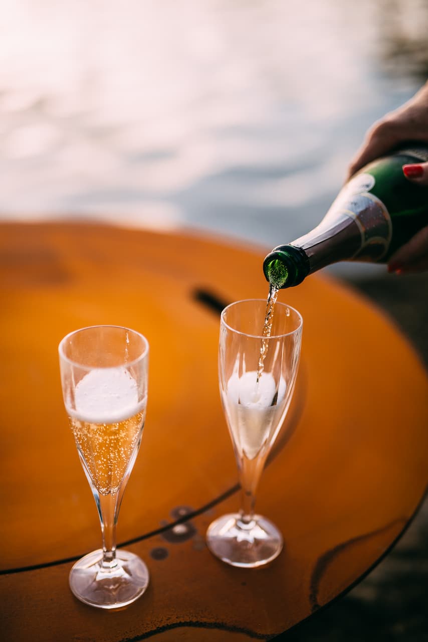 Champagne being poured into two flutes sitting on top of the lid of the Magnum 54" carbon steel fire pit.
