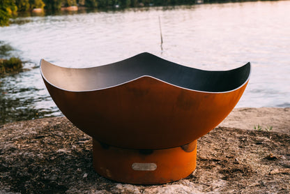 Close-up of inside the Manta Ray fire pit with curved steel edges by a lake.
