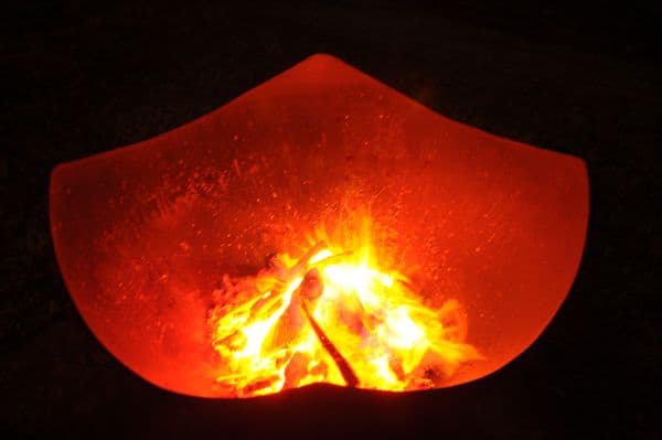 Top view of firewood glowing inside Manta Ray 36" carbon steel fire pit at night.