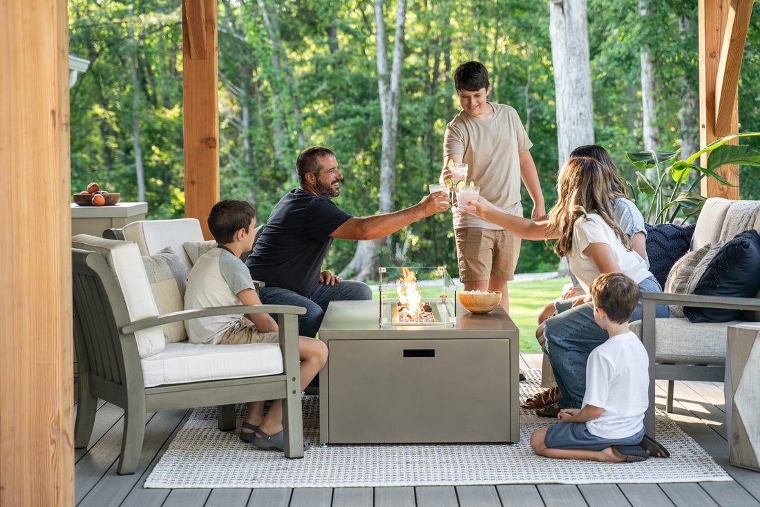 Family toasting drinks around Milan Linear propane fire table in Endura Concrete aluminum finish (wind shield sold separately).

