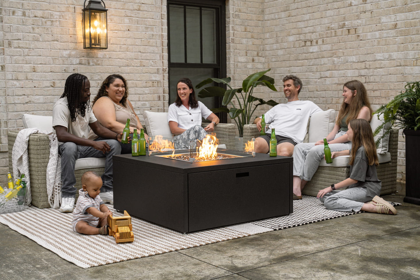Family and friends gathered around The Milan Square fire pit in Endura Graphite on a patio.