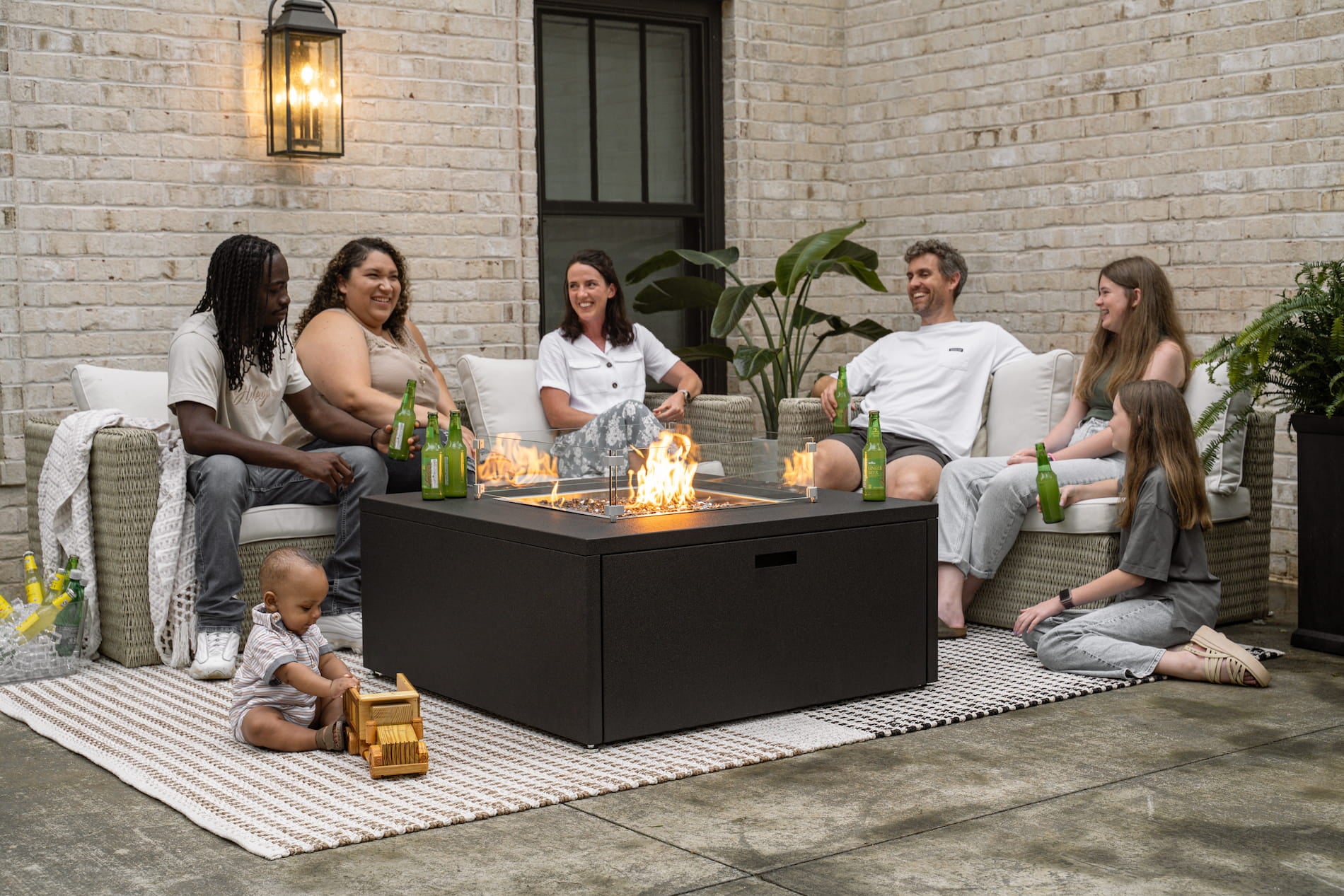 Family and friends gathered around The Milan Square fire pit in Endura Graphite on a patio.