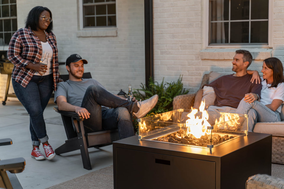 Group of friends enjoying drinks around The Milan Propane Fire Table - Square on modern patio (pictured in Endura Graphite, wind shield sold separately).

