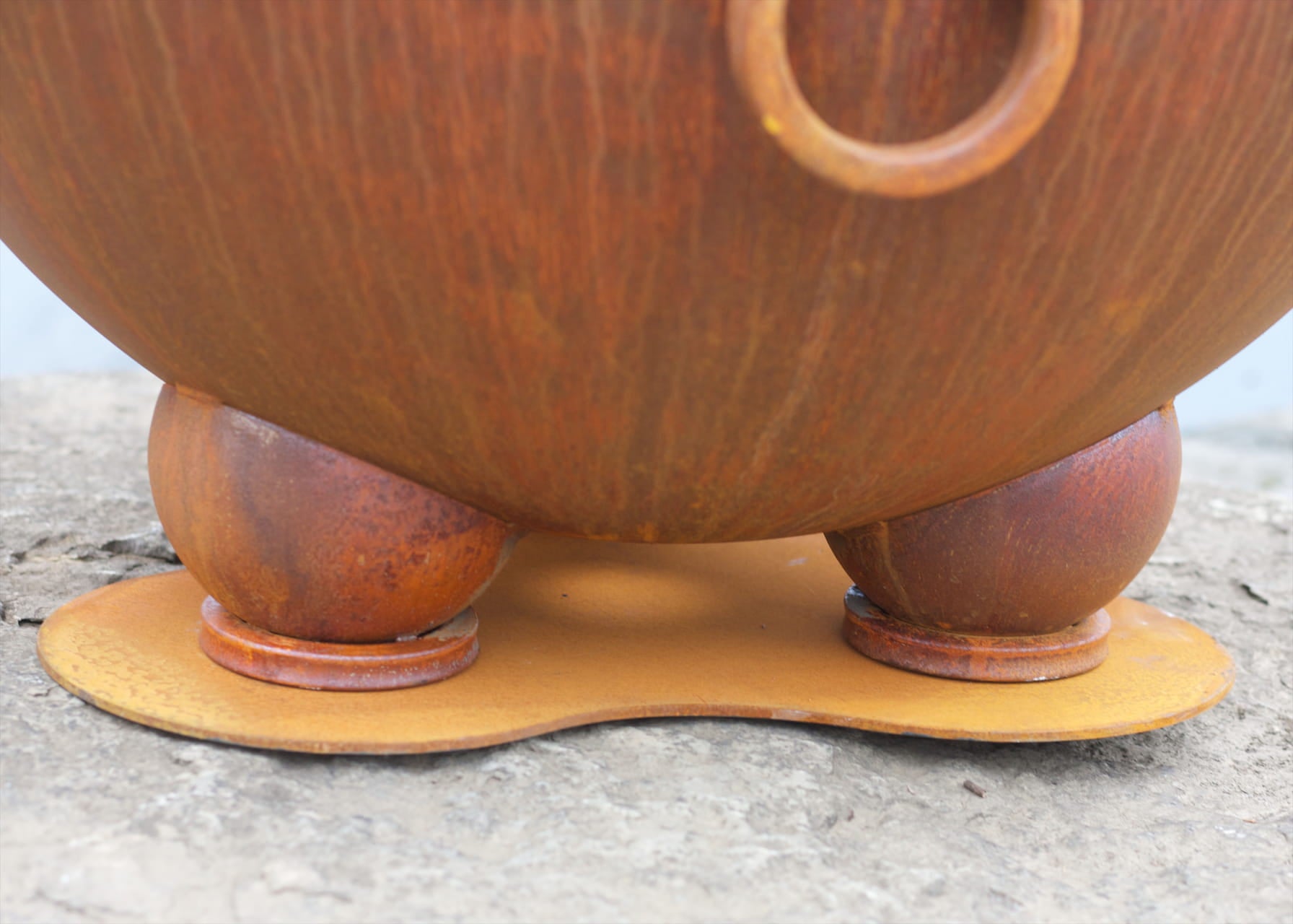 Detailed view of the Nepal fire pit's spherical feet and protective steel base plate sitting on rough stone.