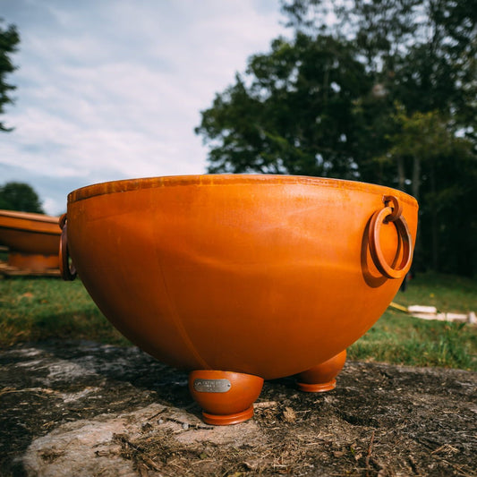 Close-up of Nepal 41" carbon fire pit showing steel ring handles and smooth bowl shape, sitting on grass.