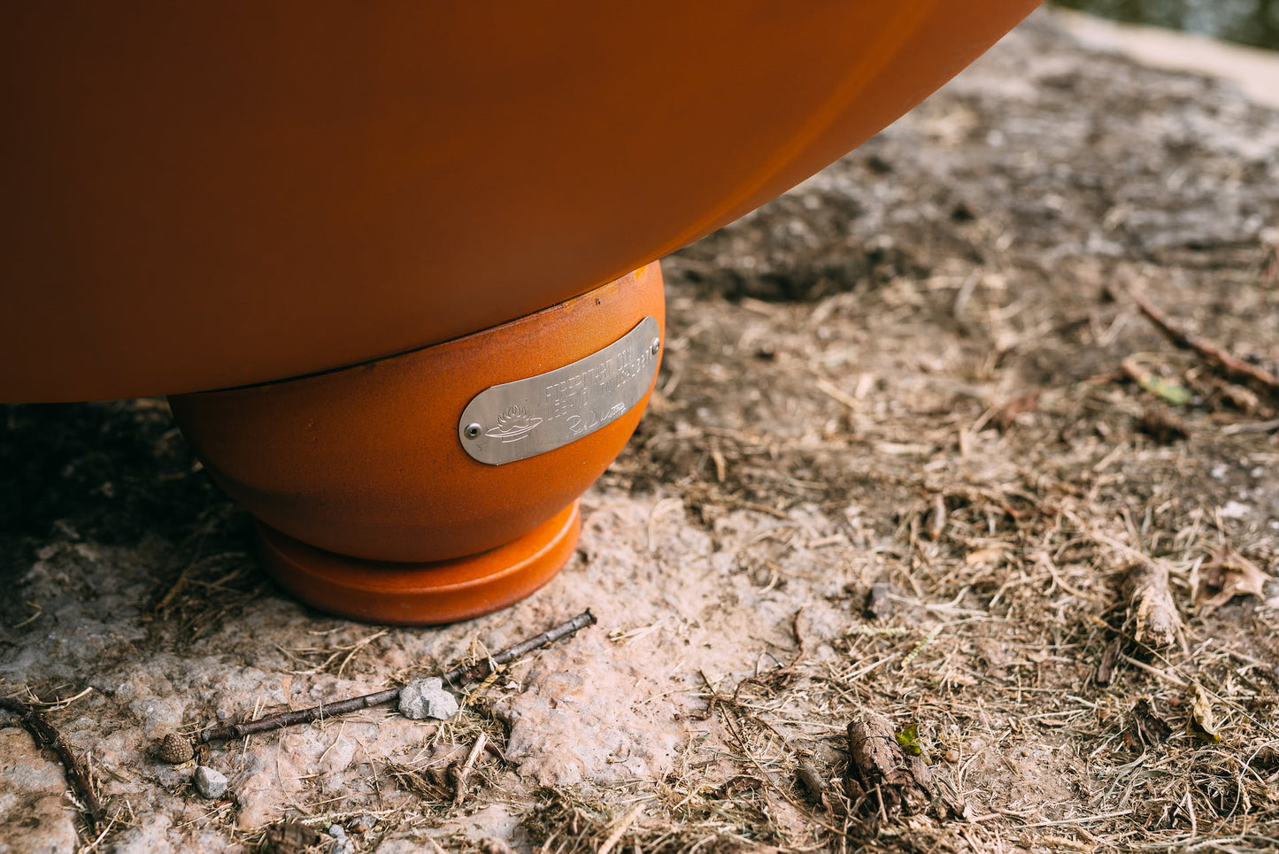 Close-up of the Nepal fire pit's rounded foot with attached Fire Pit Art® maker's tag, resting on natural stone.