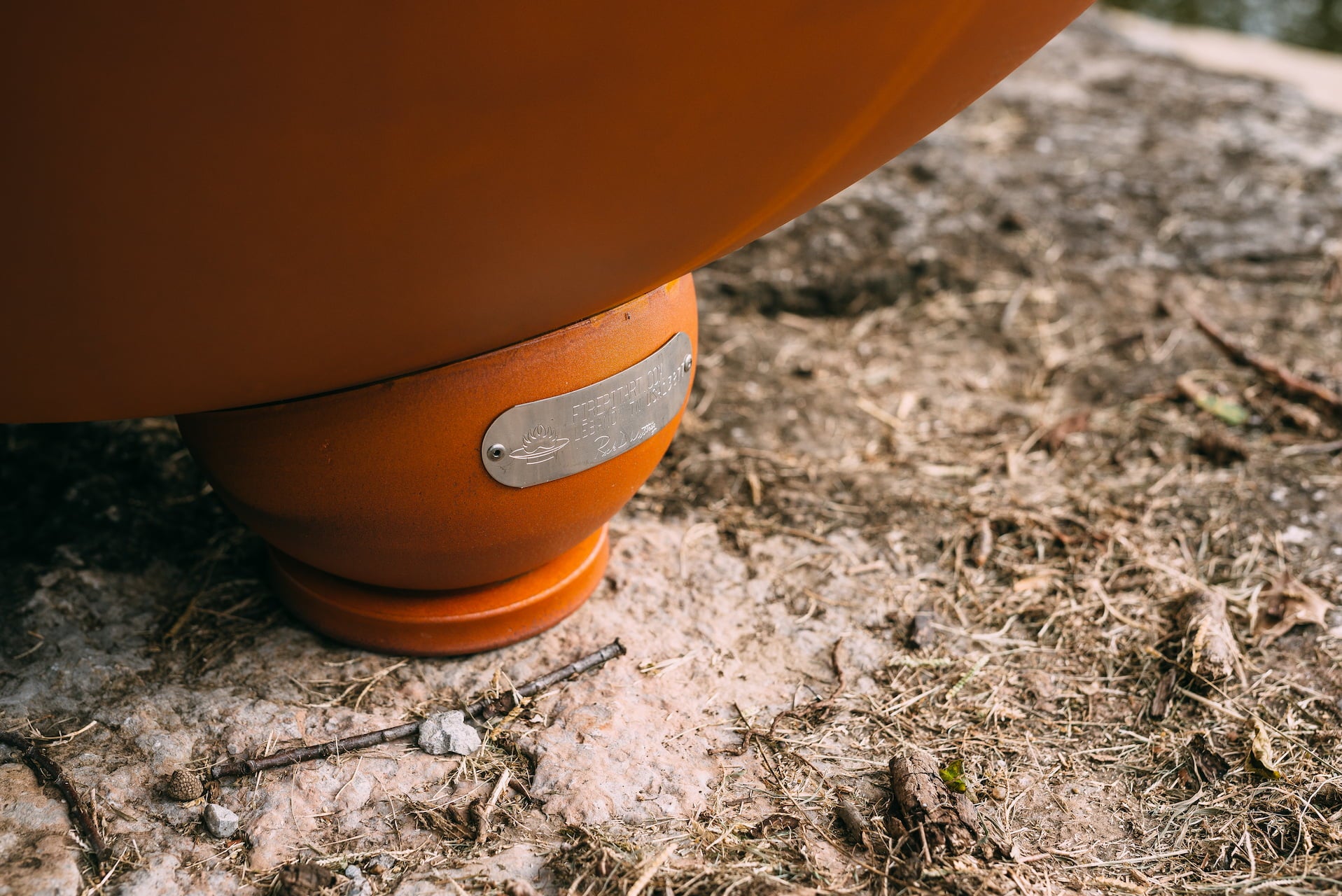 Close-up of the Nepal fire pit's rounded foot with attached Fire Pit Art® maker's tag, resting on natural stone.
