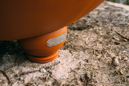 Close-up of the Nepal fire pit's rounded foot with attached Fire Pit Art® maker's tag, resting on natural stone.