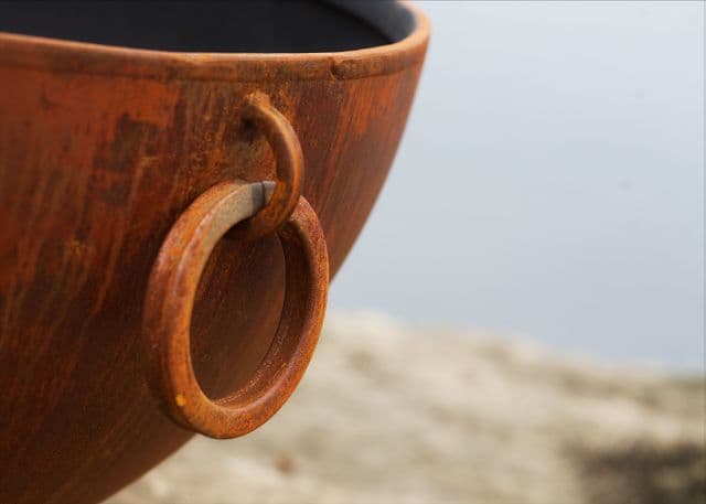 Close-up of the Nepal fire pit's rustic iron handle ring set against a smooth patina steel finish.