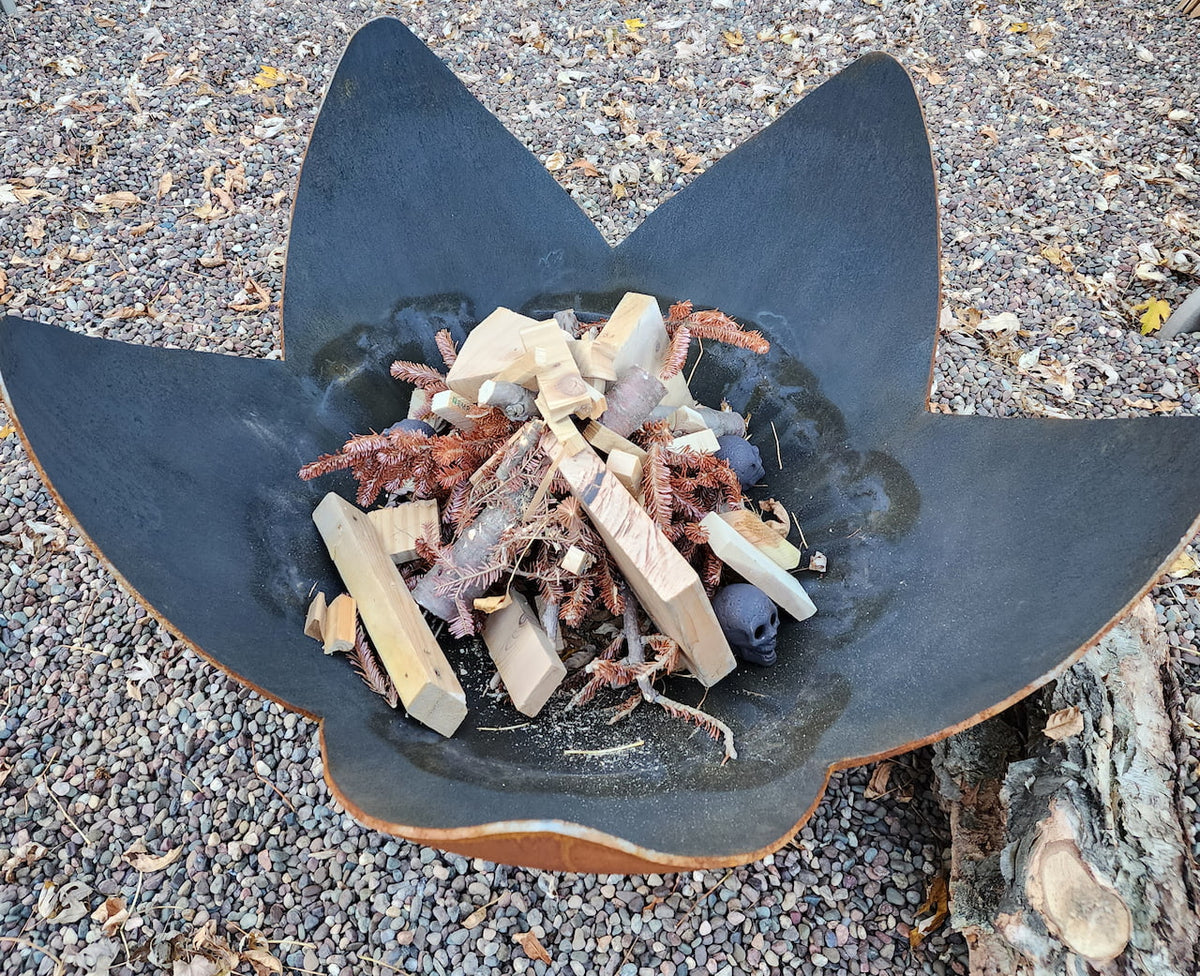 Top-down view of artisan Fire Flower bowl filled with kindling, pine branches, and Halloween props on a gravel patio.