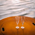 Two champagne flutes resting on the steel lid of the Saturn 41-inch fire pit, with water reflections creating a calm, elegant setting.