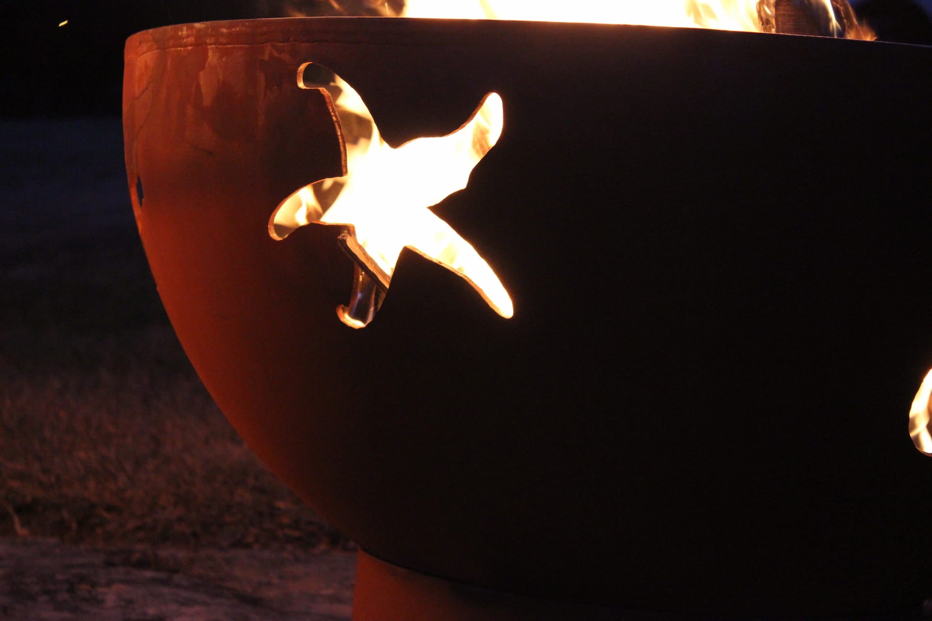 Close-up of starfish cutout illuminated by firelight on the Sea Creatures 36" carbon steel fire pit.