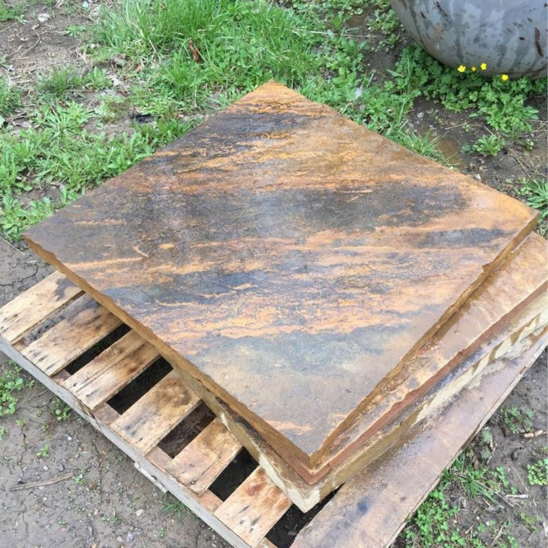 Variegated Crab Orchard stone bases stacked on a wooden pallet outdoors, showing rich golden and charcoal tones with natural texture.