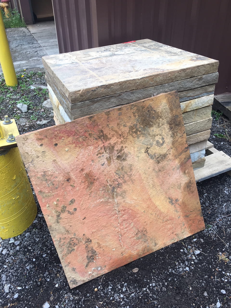 Several natural stone bases stacked beside a building, one leaning forward to show warm rust and sand-colored variations.