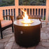 The lit Beverly round steel fire pit in copper vein powder coat on a patio.