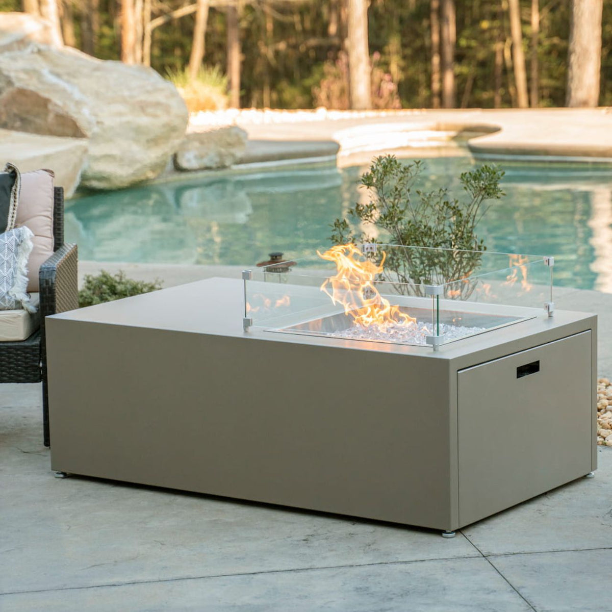 Lit Milan Offset propane fire pit table in Champagne on a patio near a pool (this color has now been retired...see new Endura colors). Made in the USA.  Wind shield sold separately.
