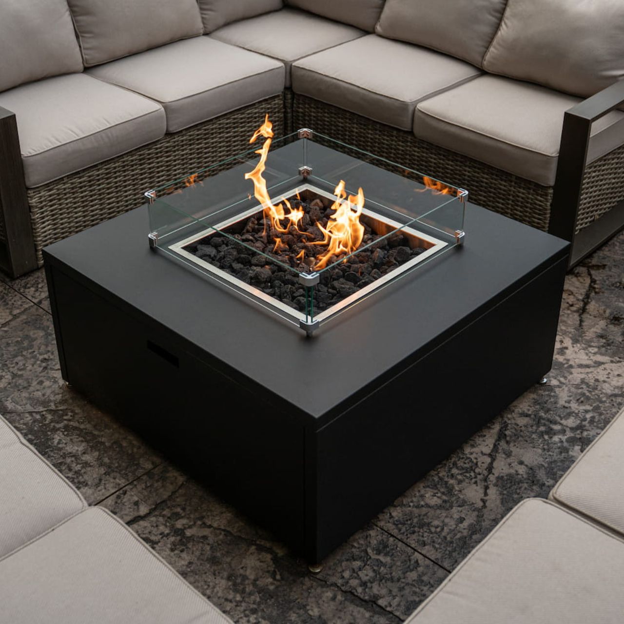 Close up of lit The Milan Propane Fire Table - Square, in Graphite, on patio (wind guard sold separately).