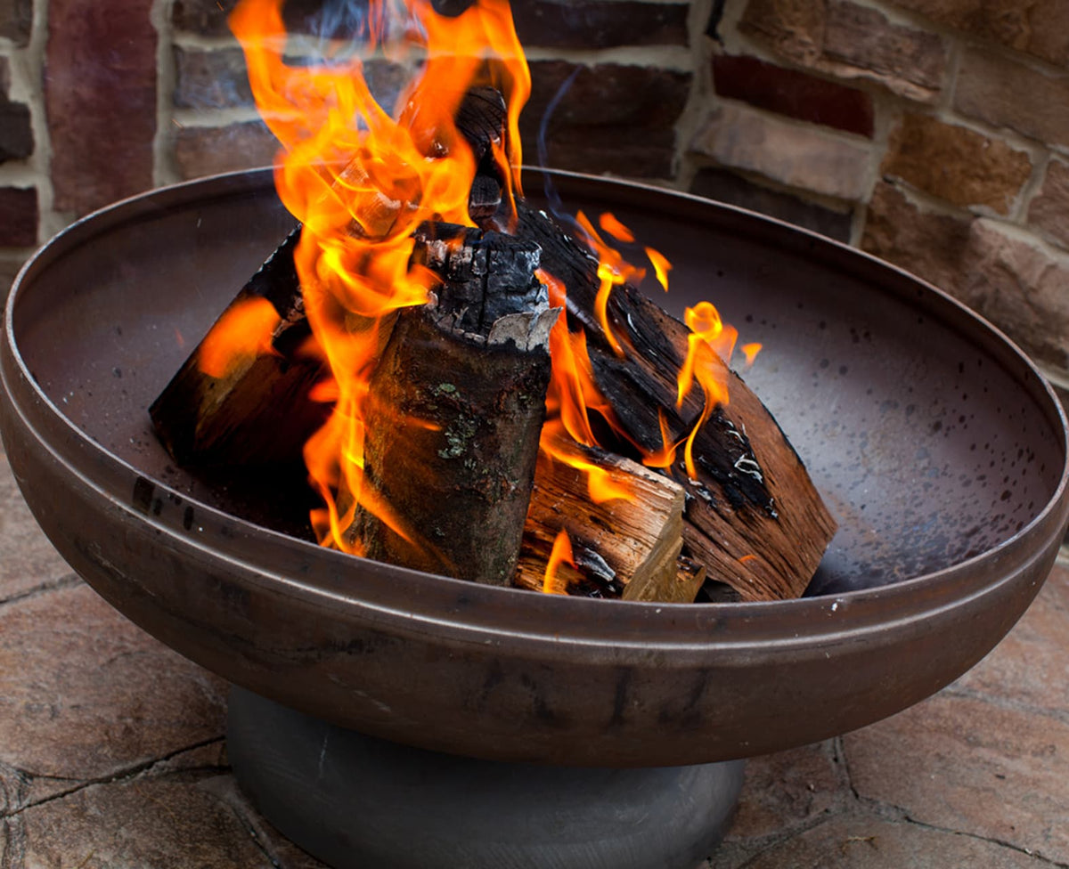 The Patriot fire pit burning bright with stacked wood on patio.