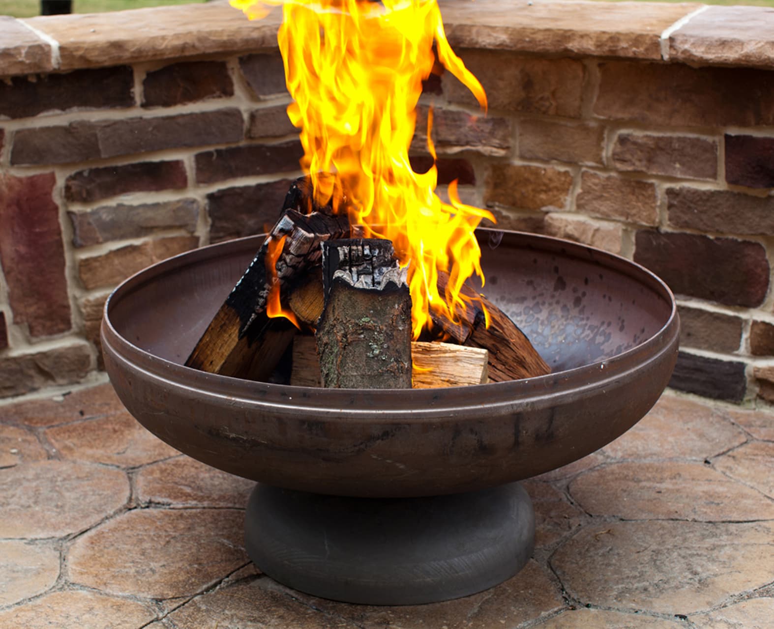 The Patriot fire pit with roaring flame against a brick wall backdrop.
