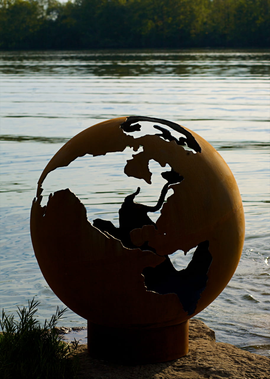 Silhouette of the Third Rock 36" carbon steel fire pit, by Fire Pit Art, with the lake as a backdrop.