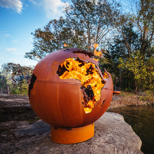 Third Rock 36-inch carbon steel fire pit glowing with fire through globe cutouts, showing Africa and Europe.  Made in USA by Fire Pit Art.
