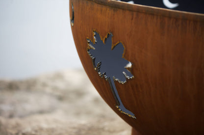 Close-up of the palm tree cutout on the Tropical Moon steel fire pit, showing the raw steel edge and weathered patina.