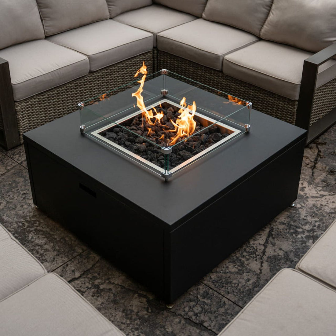 Square glass wind shield on Milan fire table, keeping flames steady outdoors. Fire table sold separately.